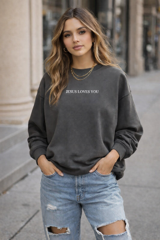 Woman wearing a dark gray sweatshirt with 'JESUS LOVES YOU' text, standing on a city street.
