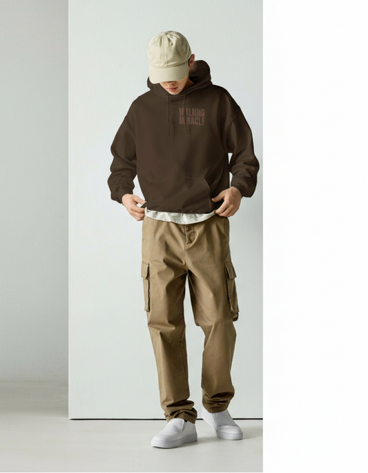 Person wearing a brown hoodie and beige pants against a white background
