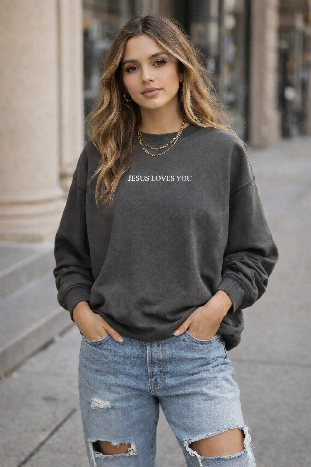 Woman wearing a dark gray sweatshirt with 'JESUS LOVES YOU' text, standing on a city street.