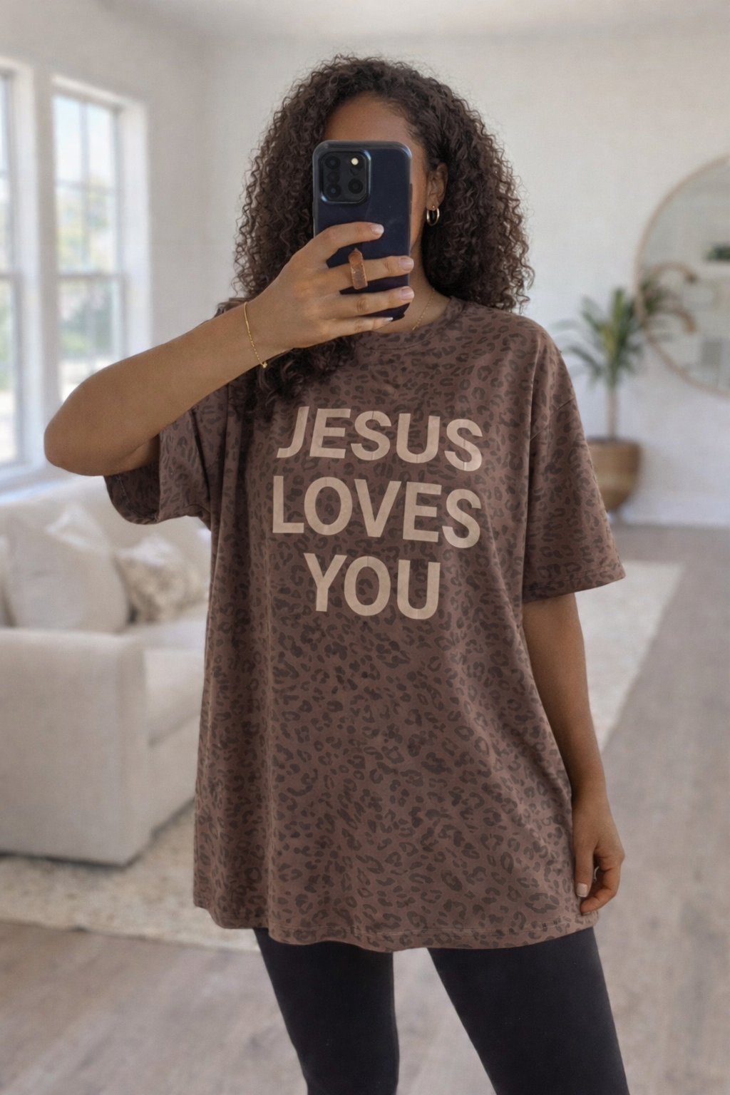 Person wearing a brown t-shirt with 'Jesus Loves You' text in a living room.