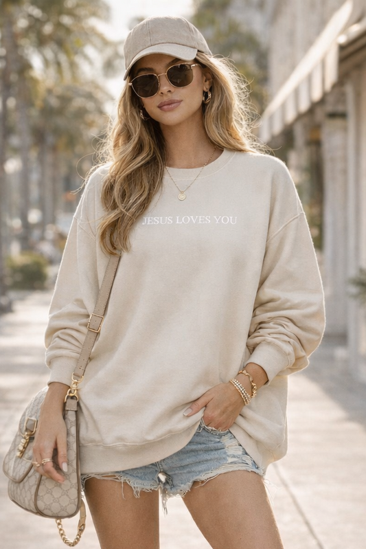 Woman in a casual outfit with a beige sweatshirt, denim shorts, and white sneakers on a sidewalk.