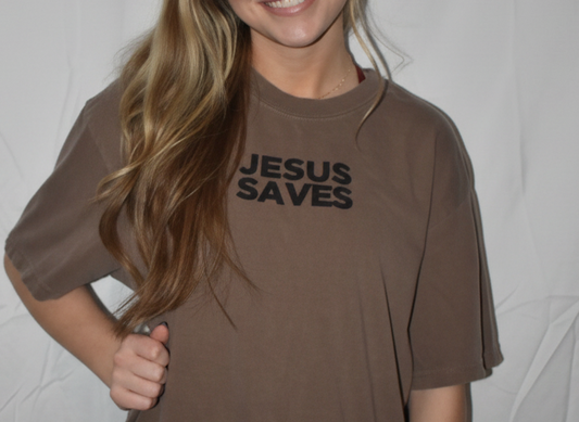 Woman wearing a brown t-shirt with 'Jesus Saves' text against a plain background