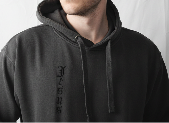 Man wearing a black hoodie with 'Jesus' printed on it against a white background