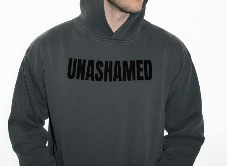Person wearing a gray hoodie with 'UNASHAMED' text on a white background