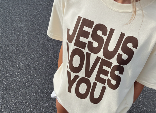Person wearing a t-shirt with 'Jesus Loves You' text on a dark background